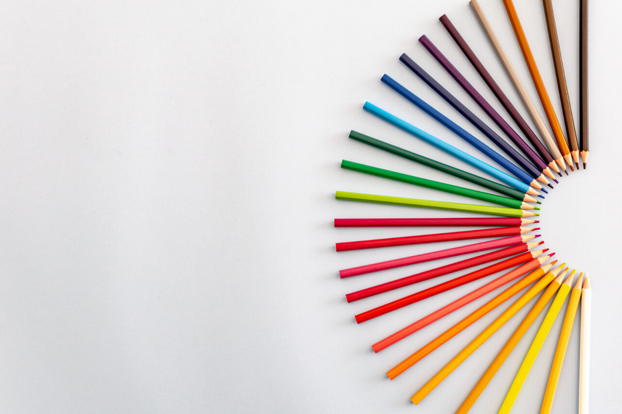 A set of colourful pencils laid out in a crescent rainbow fan shape on the right of the image on a grey background desktop wallpaper